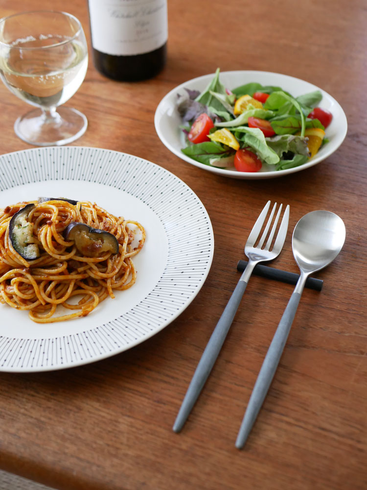 ブラウンゴールドまたはグレーシルバーの【Cutipol MIO カトラリー】セットがテーブルに整然と並べられ、料理と共に展示されている様子