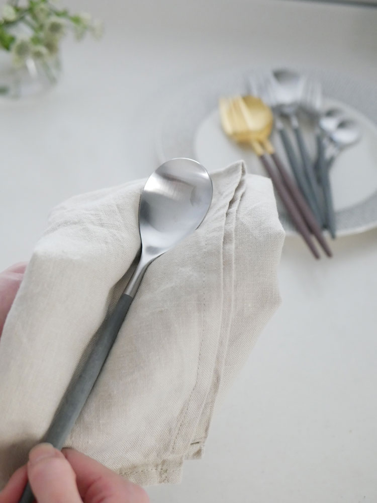 クチポール MIOブランドのブラウンゴールドおよびグレーシルバーのカトラリーセットが、テーブルクロスの上に整然と並べられたダイニングテーブルの画像