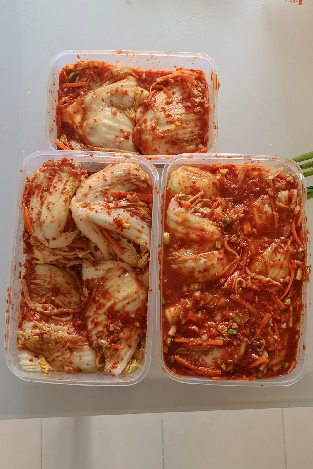 Three plastic containers of homemade kimchi coated in red chili paste