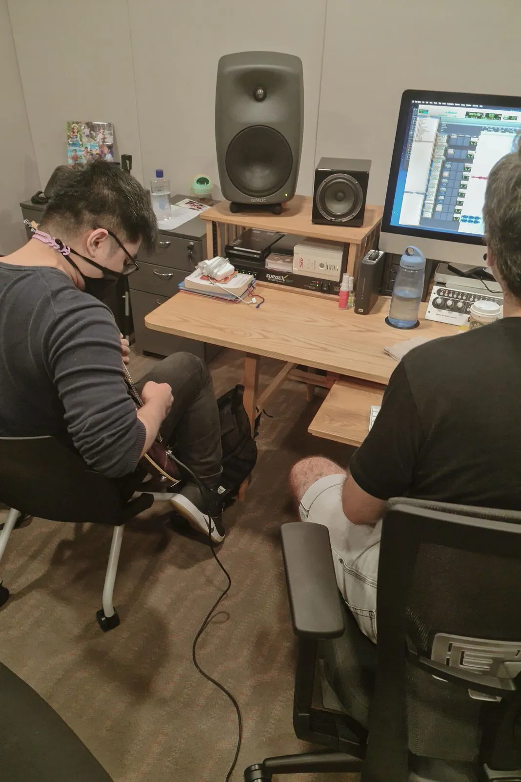 Two people in a recording studio, one playing guitar, one at a computer