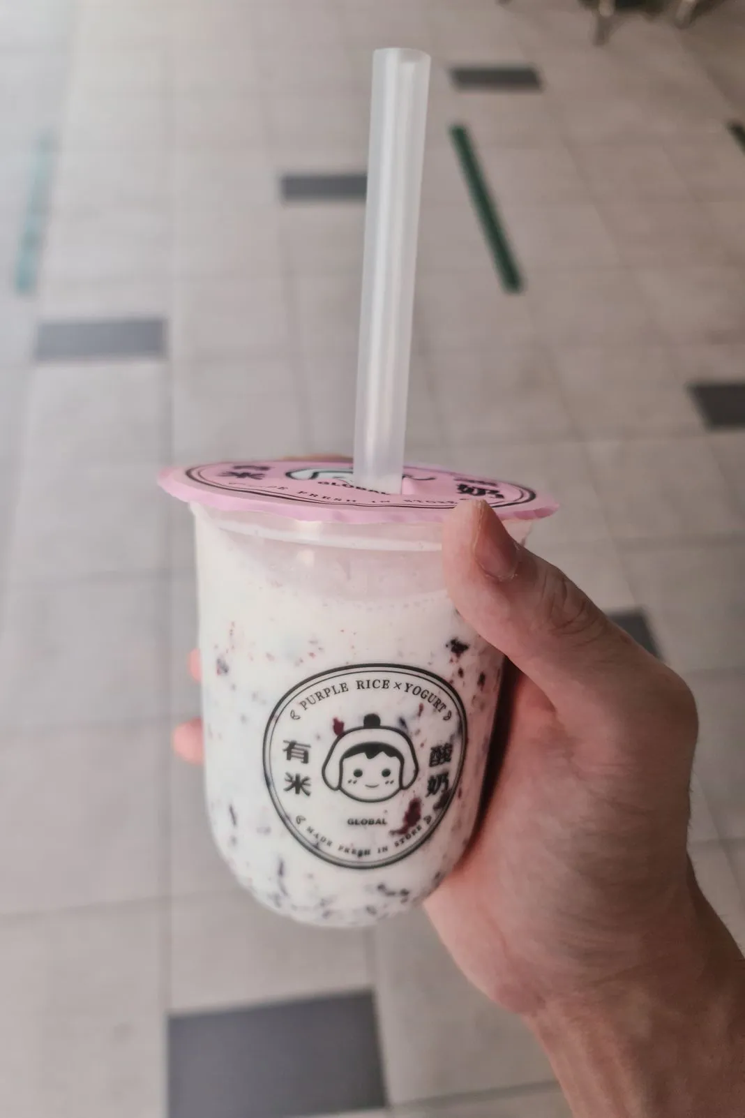 A hand holding a purple rice and yogurt drink with a straw