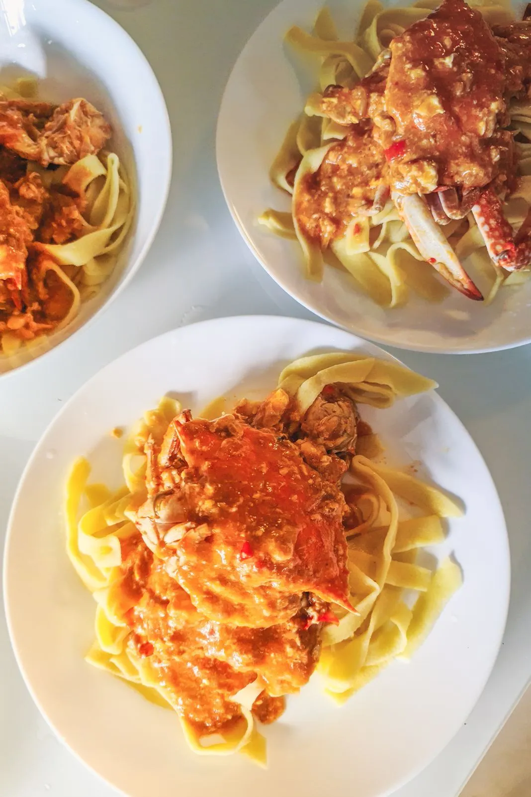 Three plates of pasta topped with whole chili crab, seen from above
