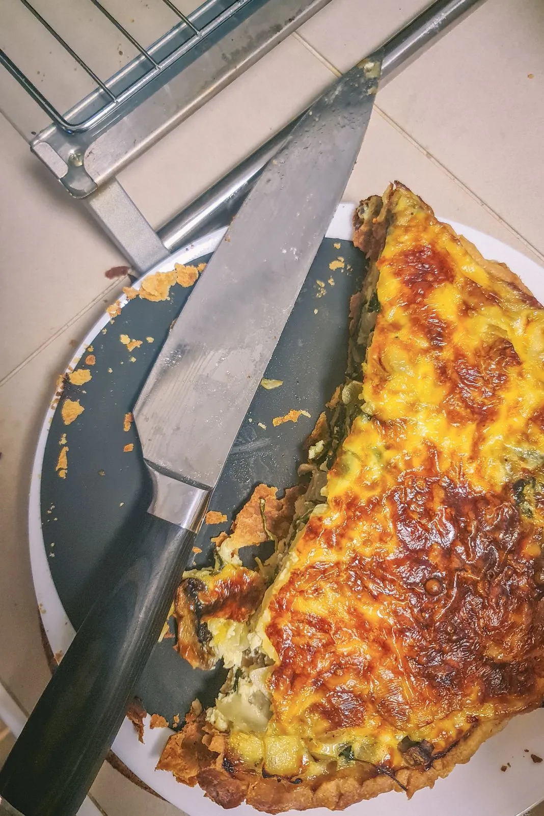 A knife slicing into a cheesy baked quiche on a plate