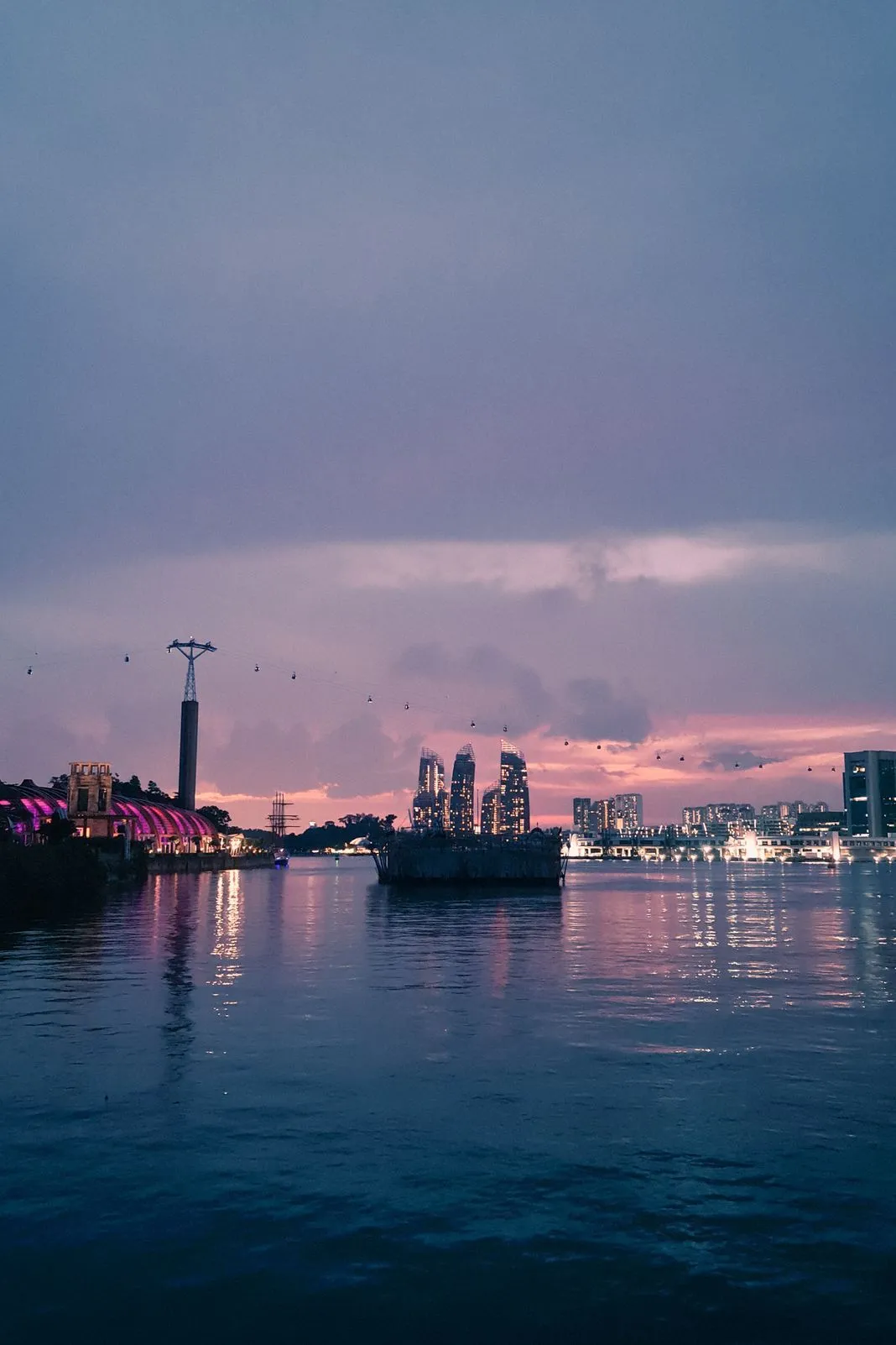 Skyscrapers under construction across a harbor with a cable car line, pink dusk sky