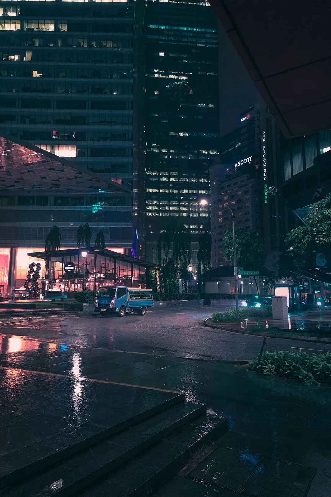 A small truck on a rain-slicked city street lined with lit skyscrapers at night