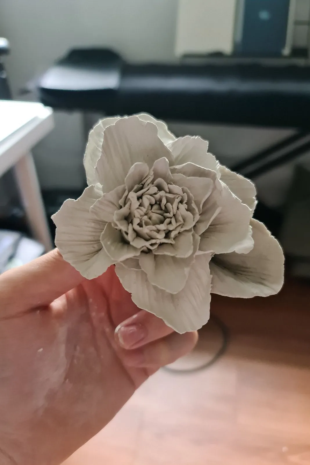 A hand holding a delicate white clay flower sculpture indoors