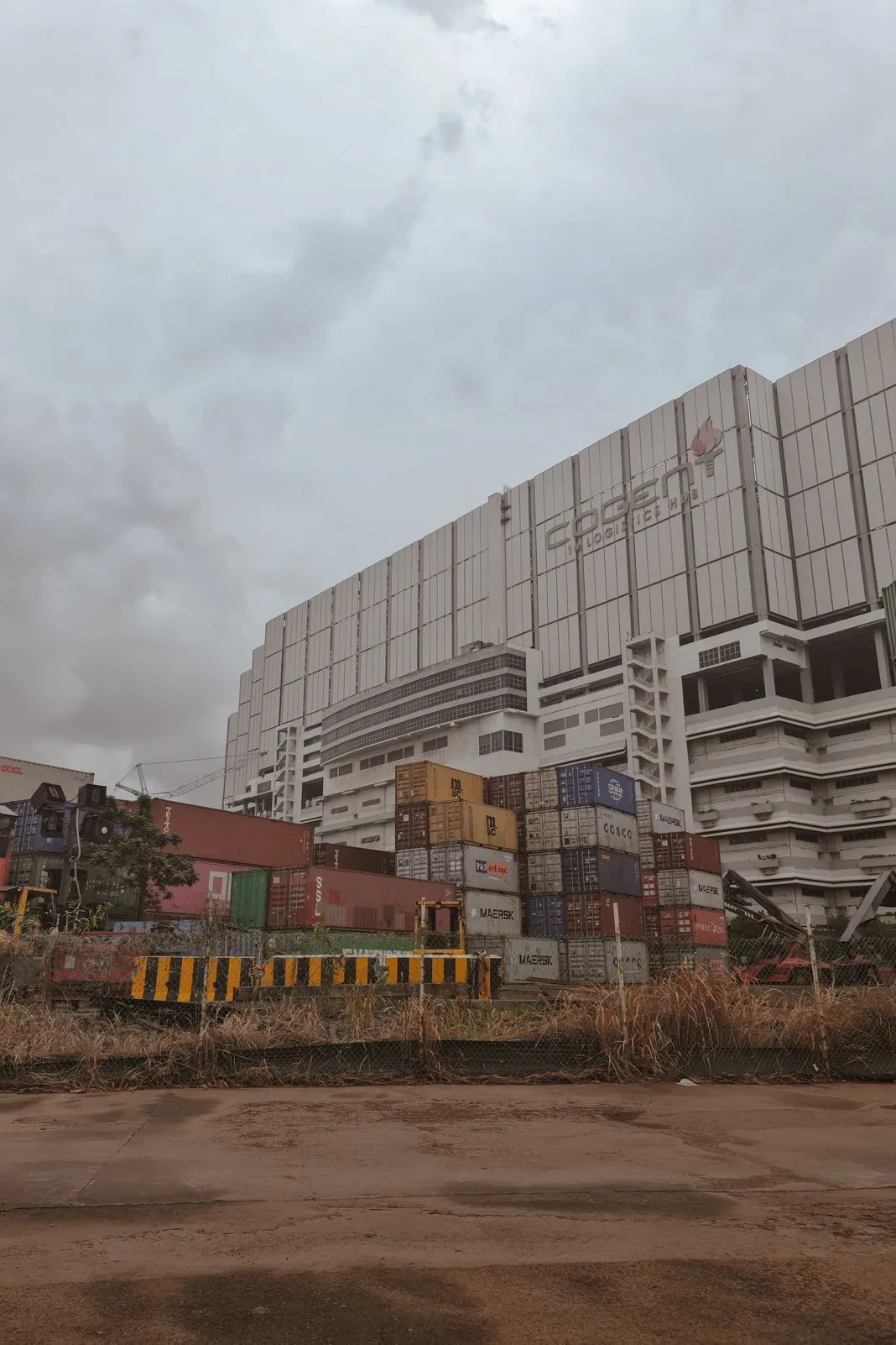 Stacked shipping containers in front of a large logistics hub building