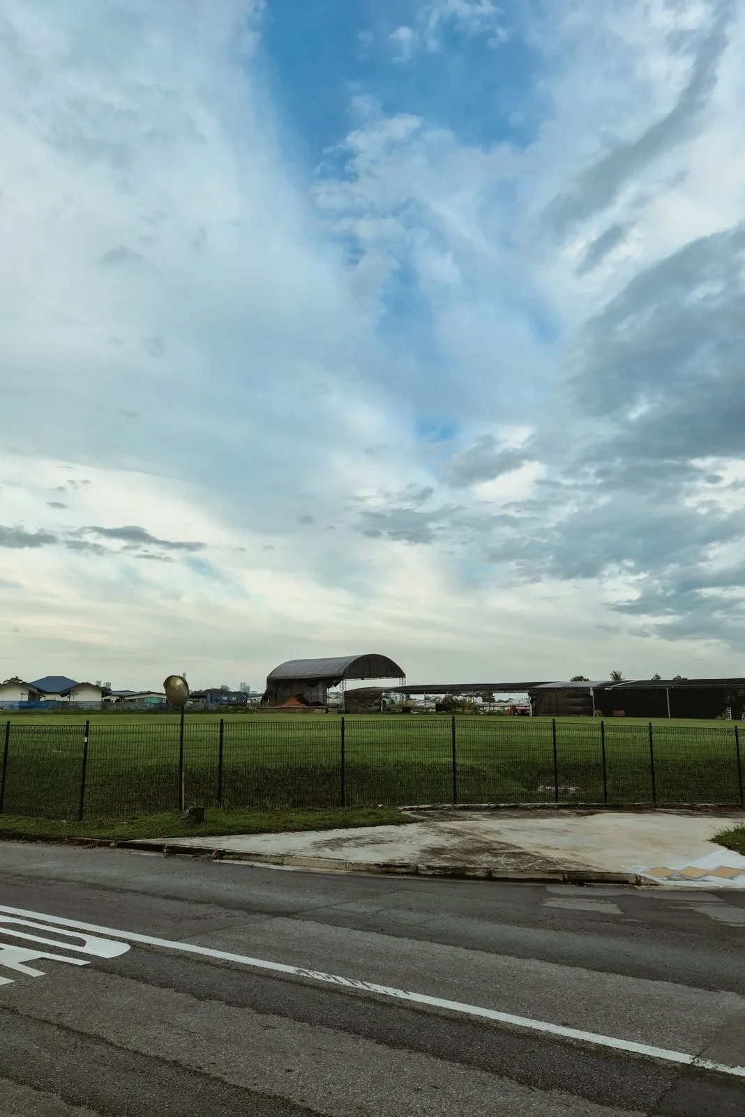 A wide cloudy sky over a grassy field with covered outdoor structures