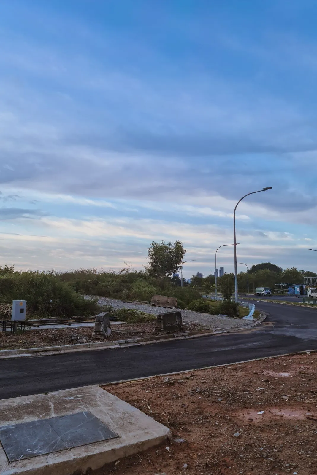 A newly paved road under construction with barriers and a city skyline beyond