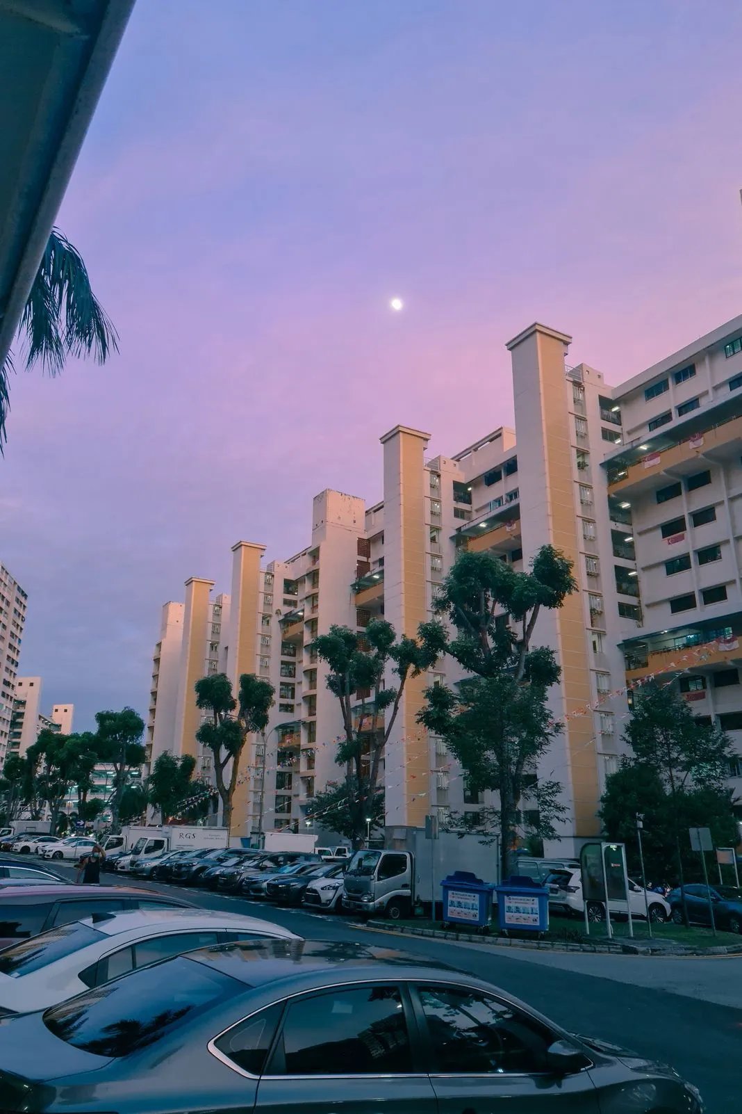 Apartment blocks strung with festive bunting under a pink dusk sky with the moon