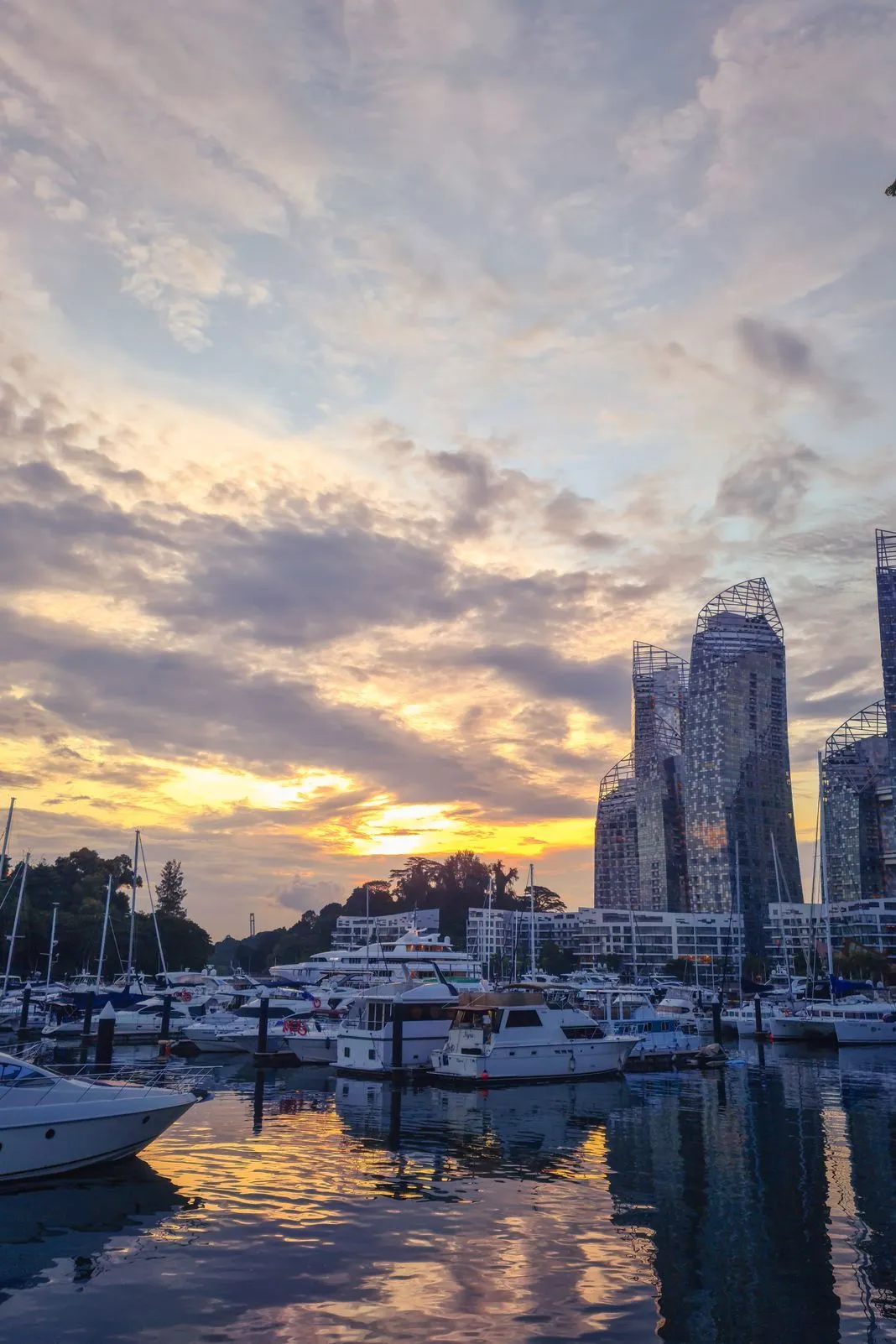 Yachts docked in a marina beneath skyscrapers under construction at sunset