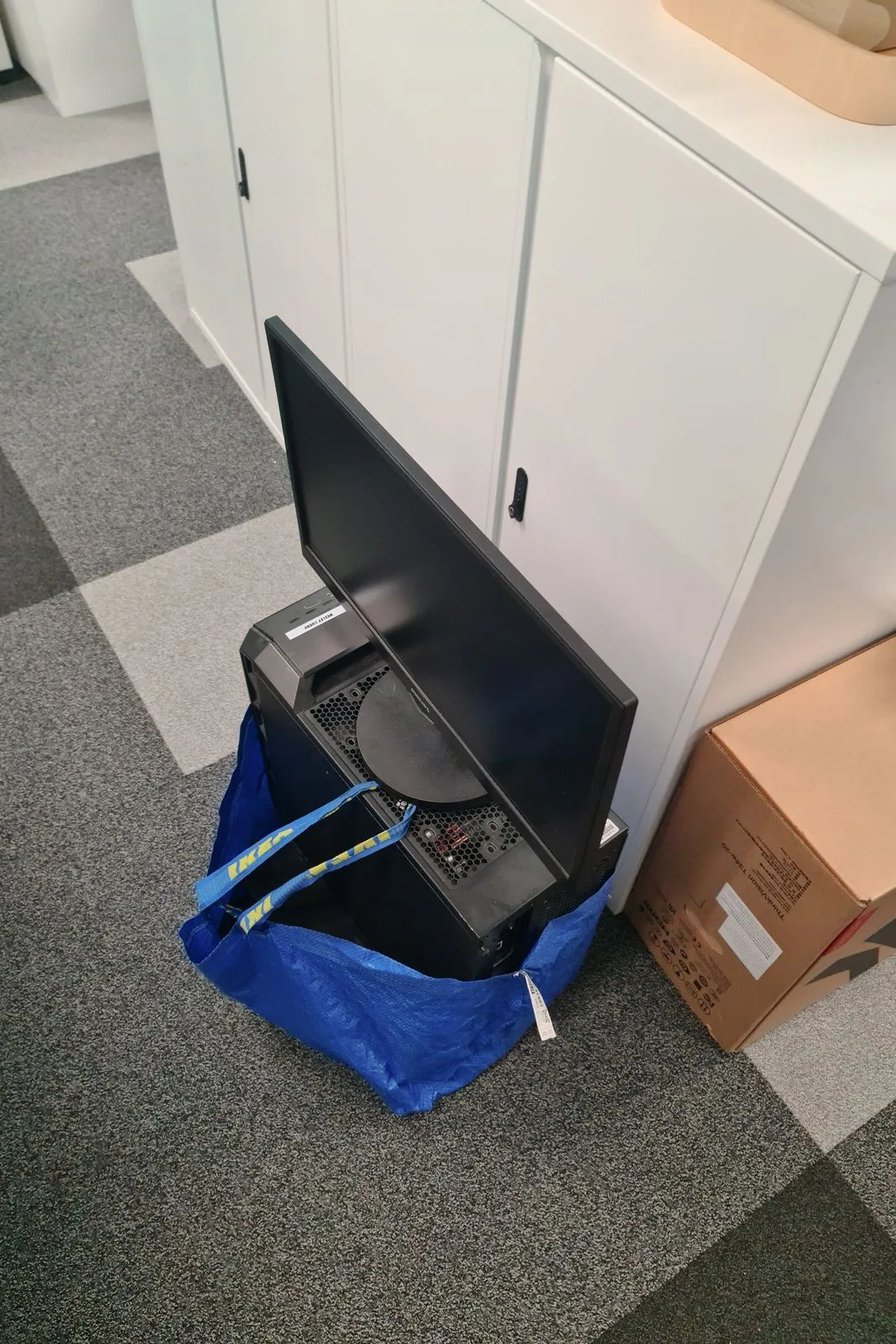 A desktop computer and monitor packed into a blue IKEA bag beside moving boxes