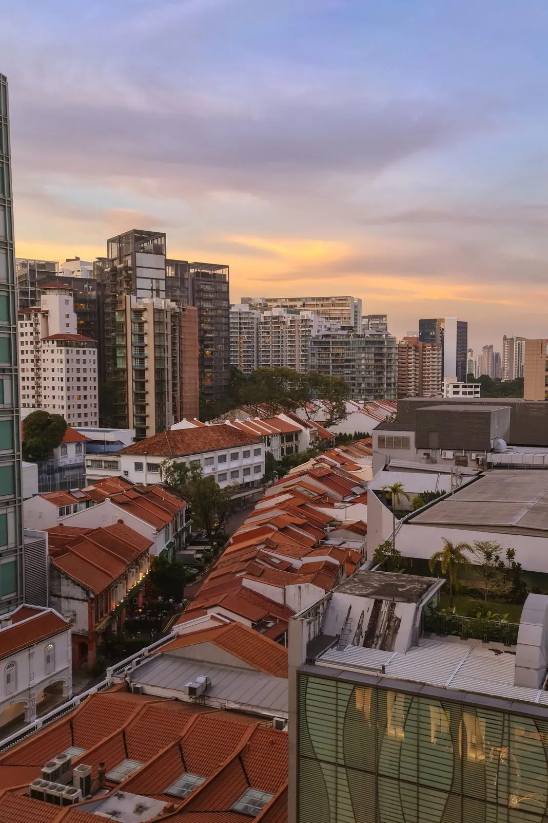 Rows of red-roofed shophouses beneath high-rise apartments at sunset