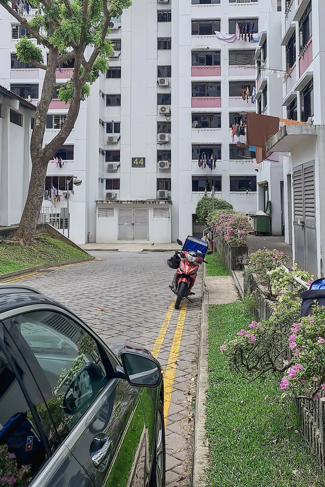 A parked motorbike outside an HDB block with laundry hanging and bougainvillea