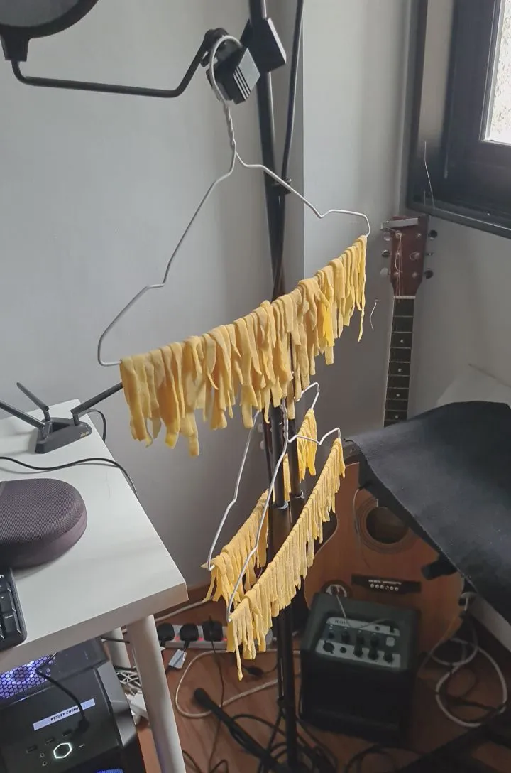 Fresh pasta noodles hanging to dry on wire hangers beside a guitar