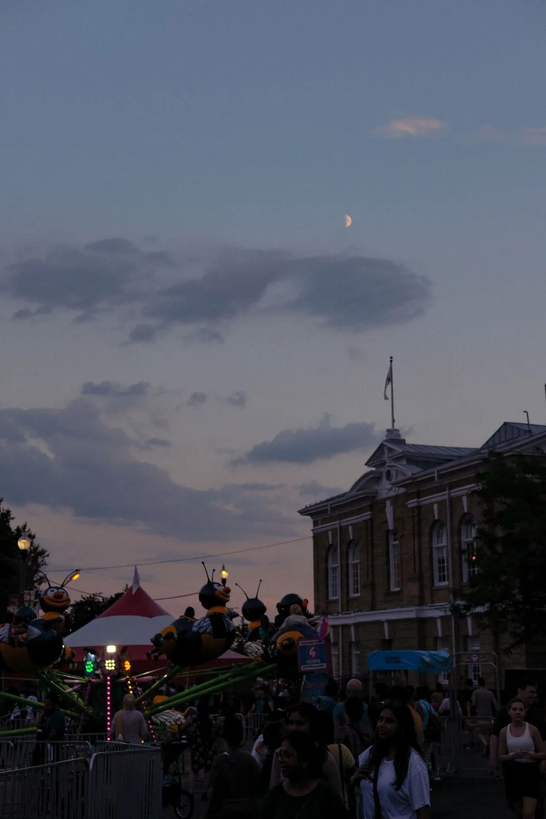 Crescent moon rising above a historic building over an evening fairground crowd