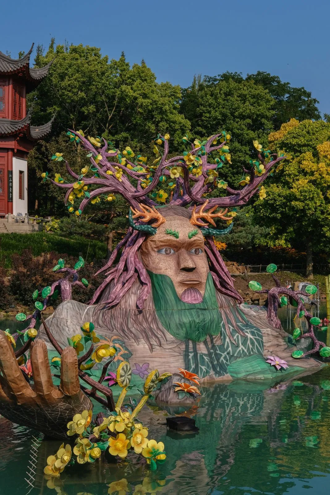 Illuminated lantern sculpture of a mythical face rising from a garden pond