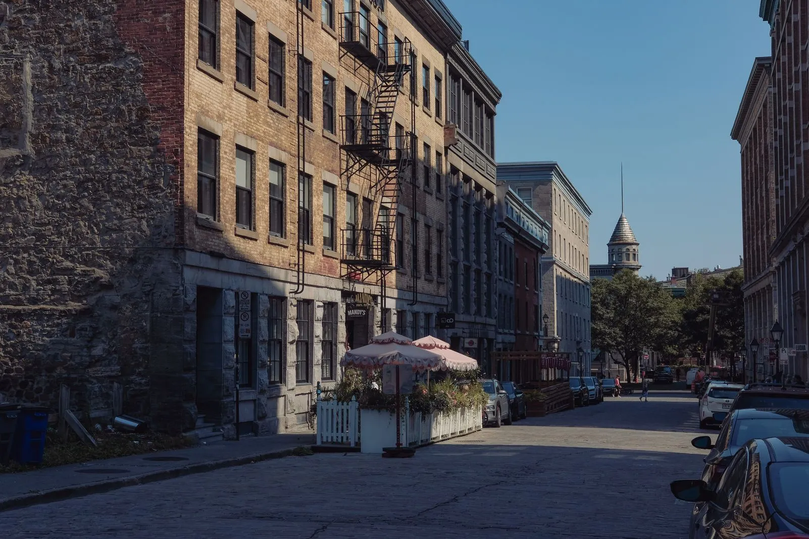 Cobblestone street lined with old stone buildings and a domed tower in the distance
