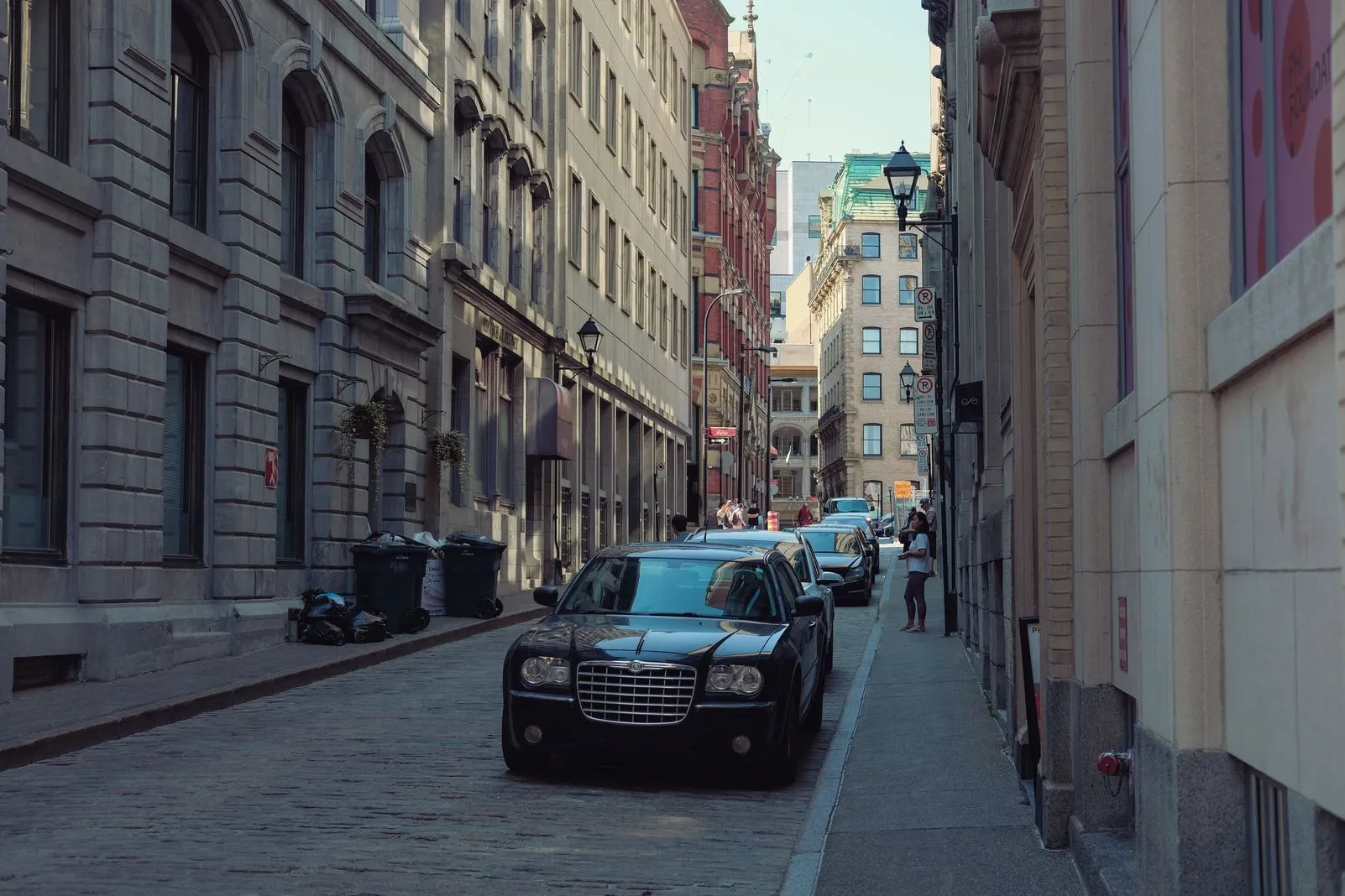 Black car driving down a narrow cobblestone street between historic buildings
