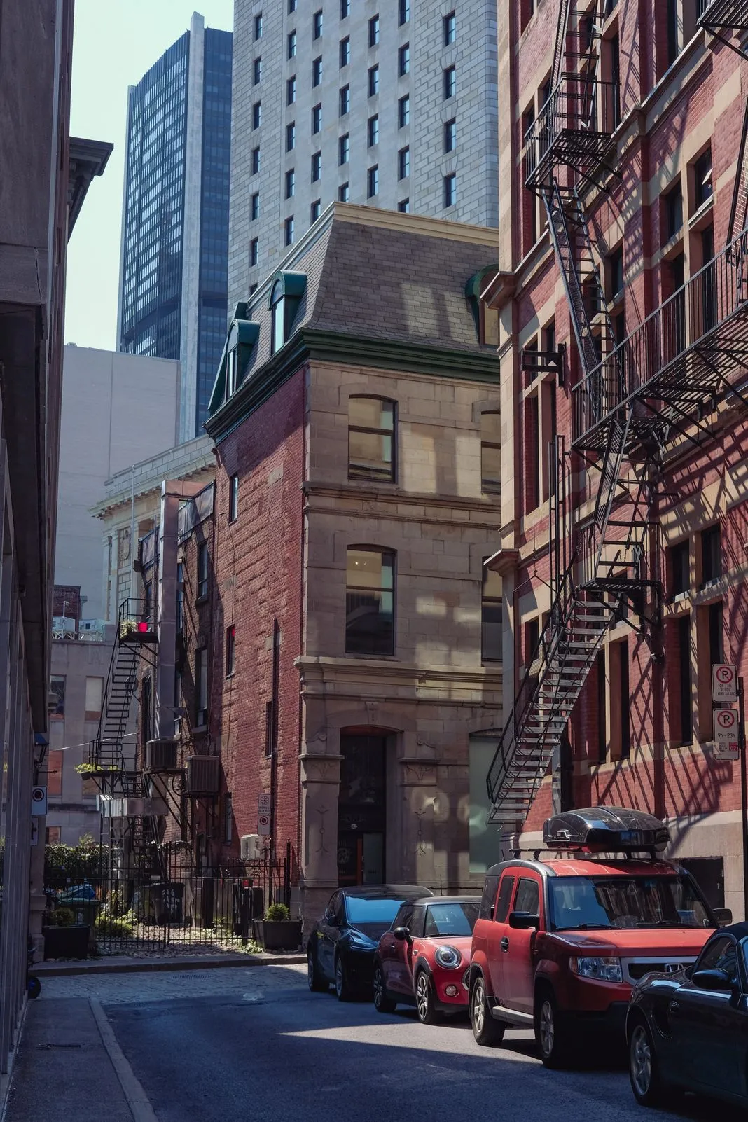 Narrow street between a red brick building with fire escapes and glass towers