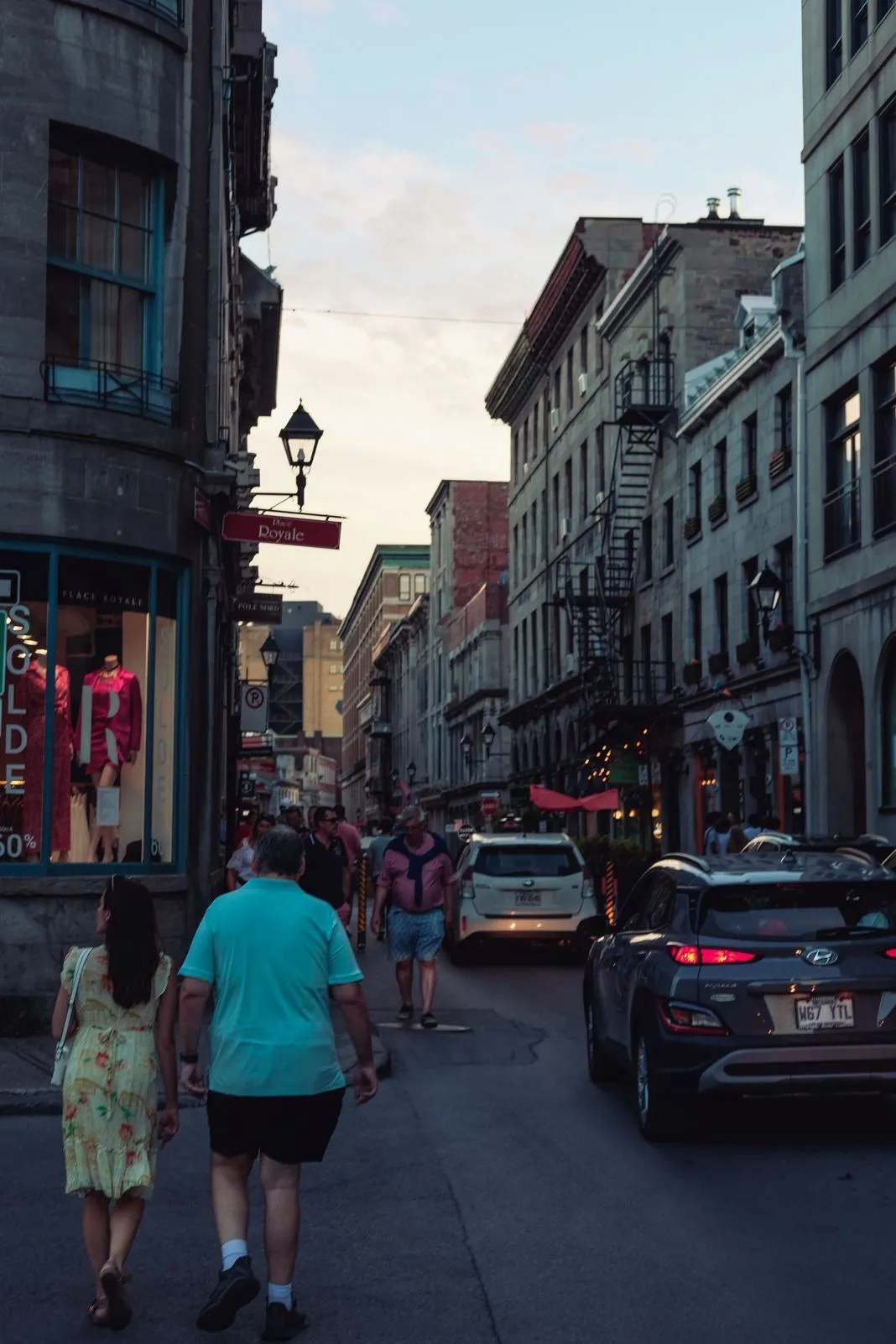 Couple walking past shops on a historic street lined with old stone buildings at dusk