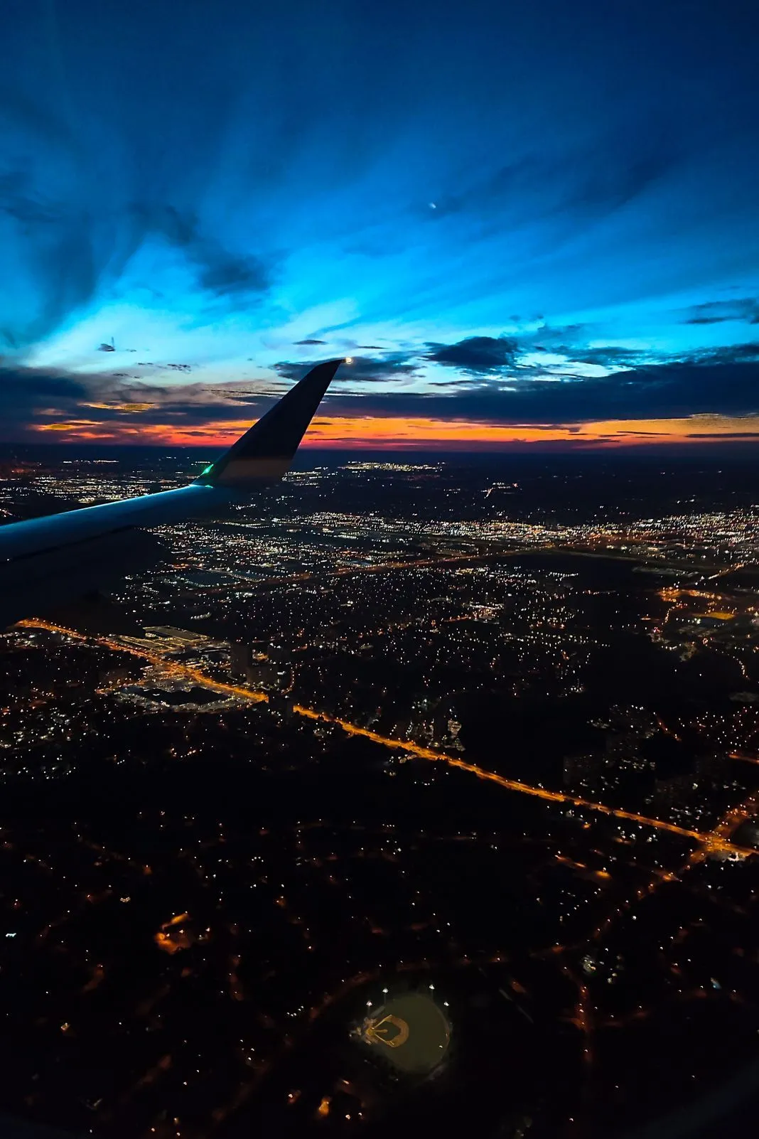 Airplane wing silhouetted against a colorful dusk sky over a city skyline