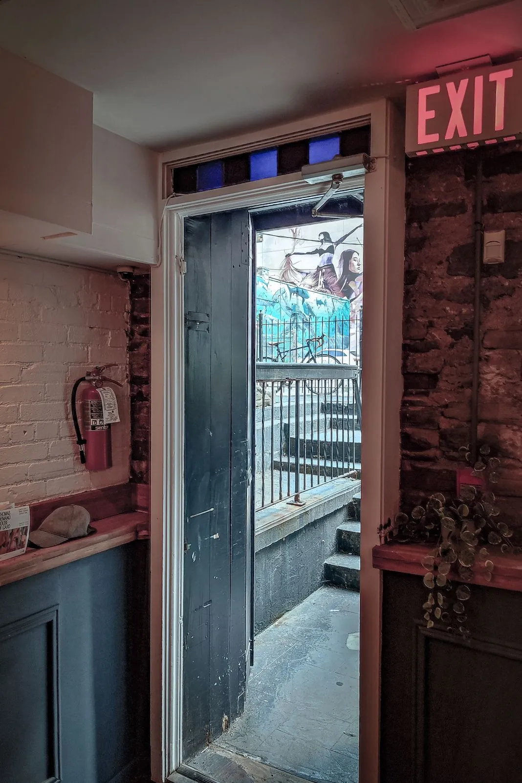Open doorway leading to an alley with a mural, seen past an EXIT sign