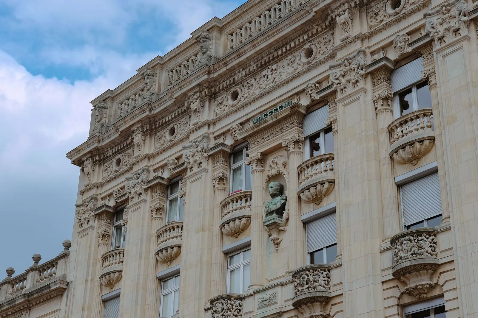 Close-up of an ornate stone facade with carved figures, balconies, and a bronze bust