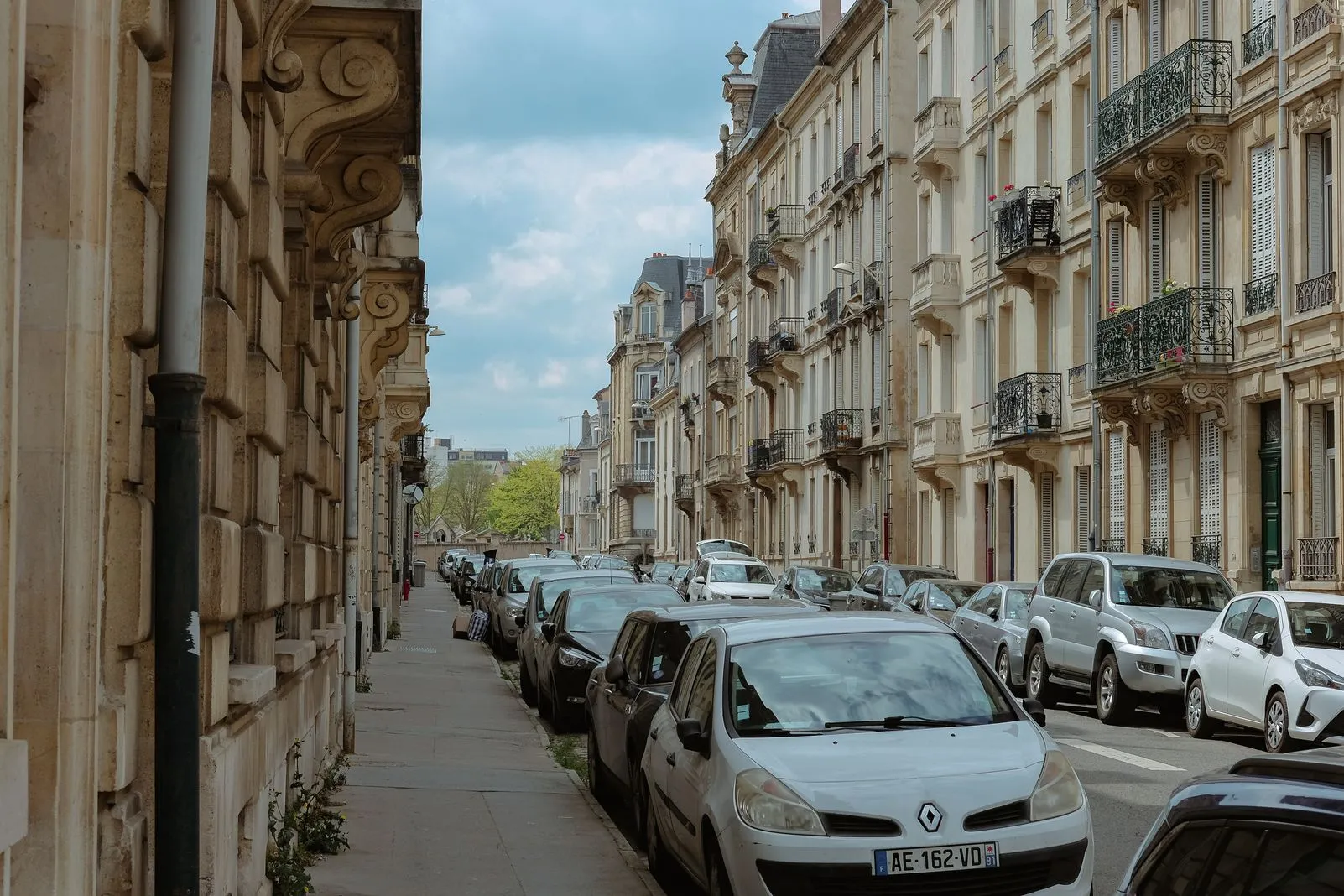 Cars parked along a narrow street lined with elegant balconied apartment buildings