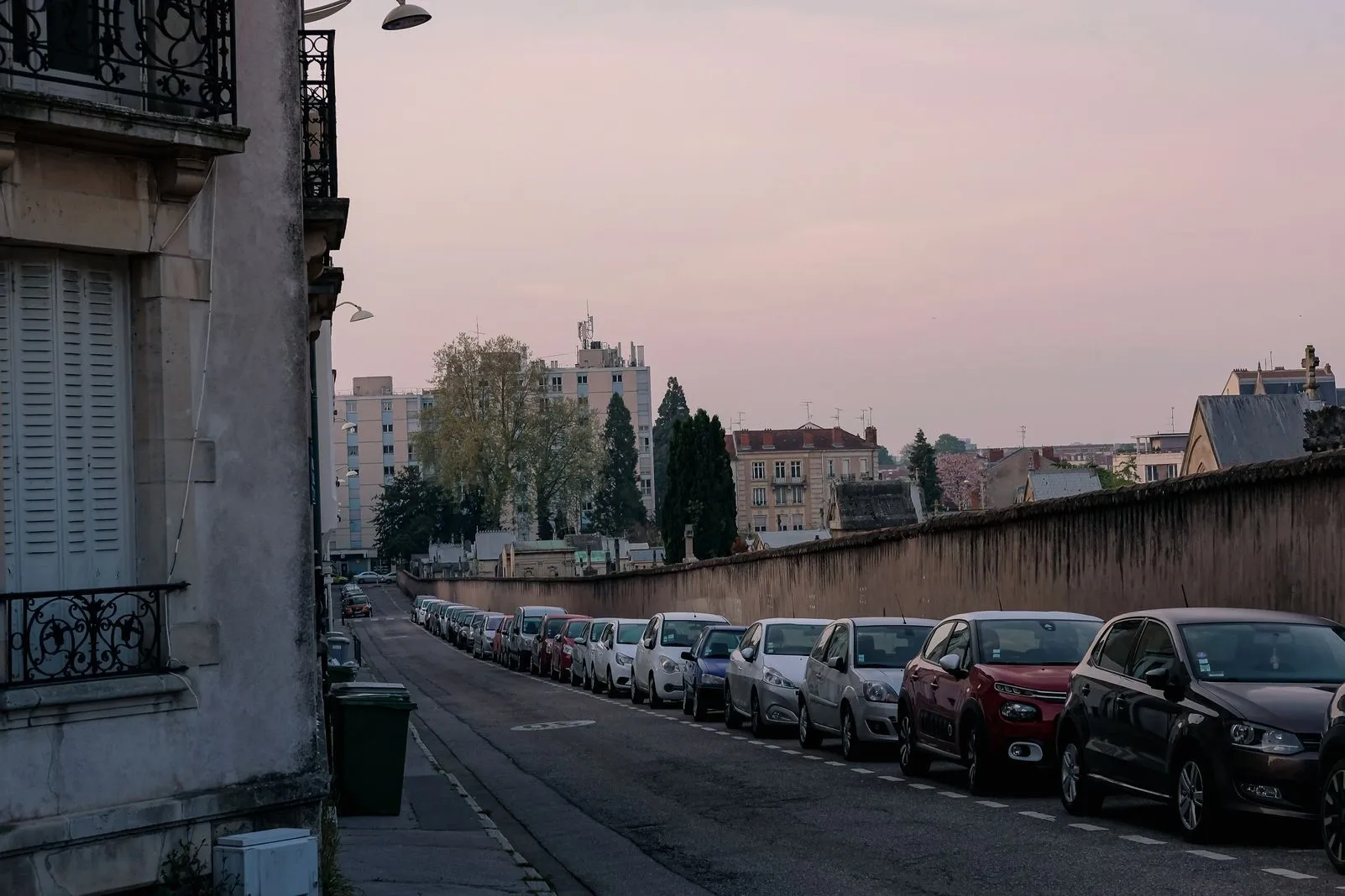 Cars parked along a street at dusk under a pink-tinted sky
