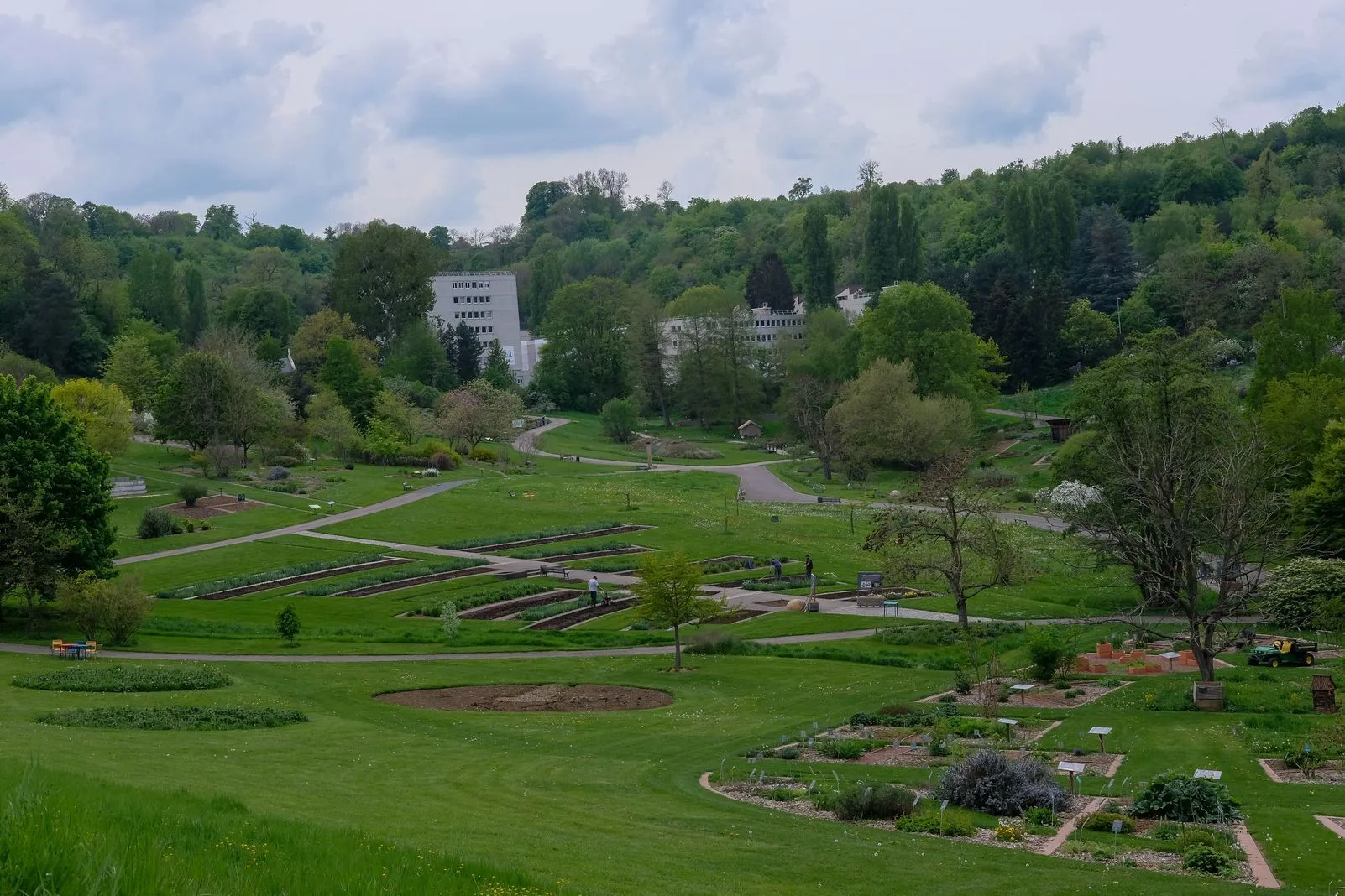Aerial view of a botanical garden with manicured lawns, plant beds, and wooded hills beyond