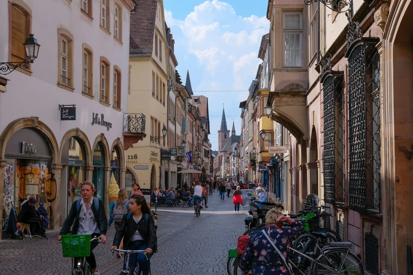 Cyclists ride through a cobbled shopping street lined with half-timbered buildings