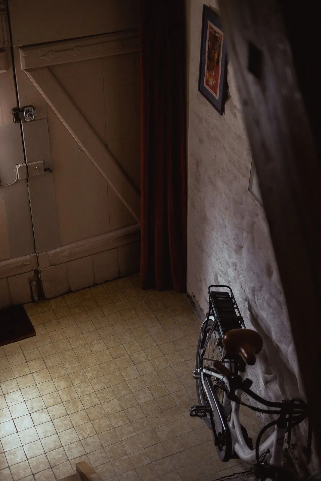 A bicycle leaning against a wall inside a dim tiled entryway