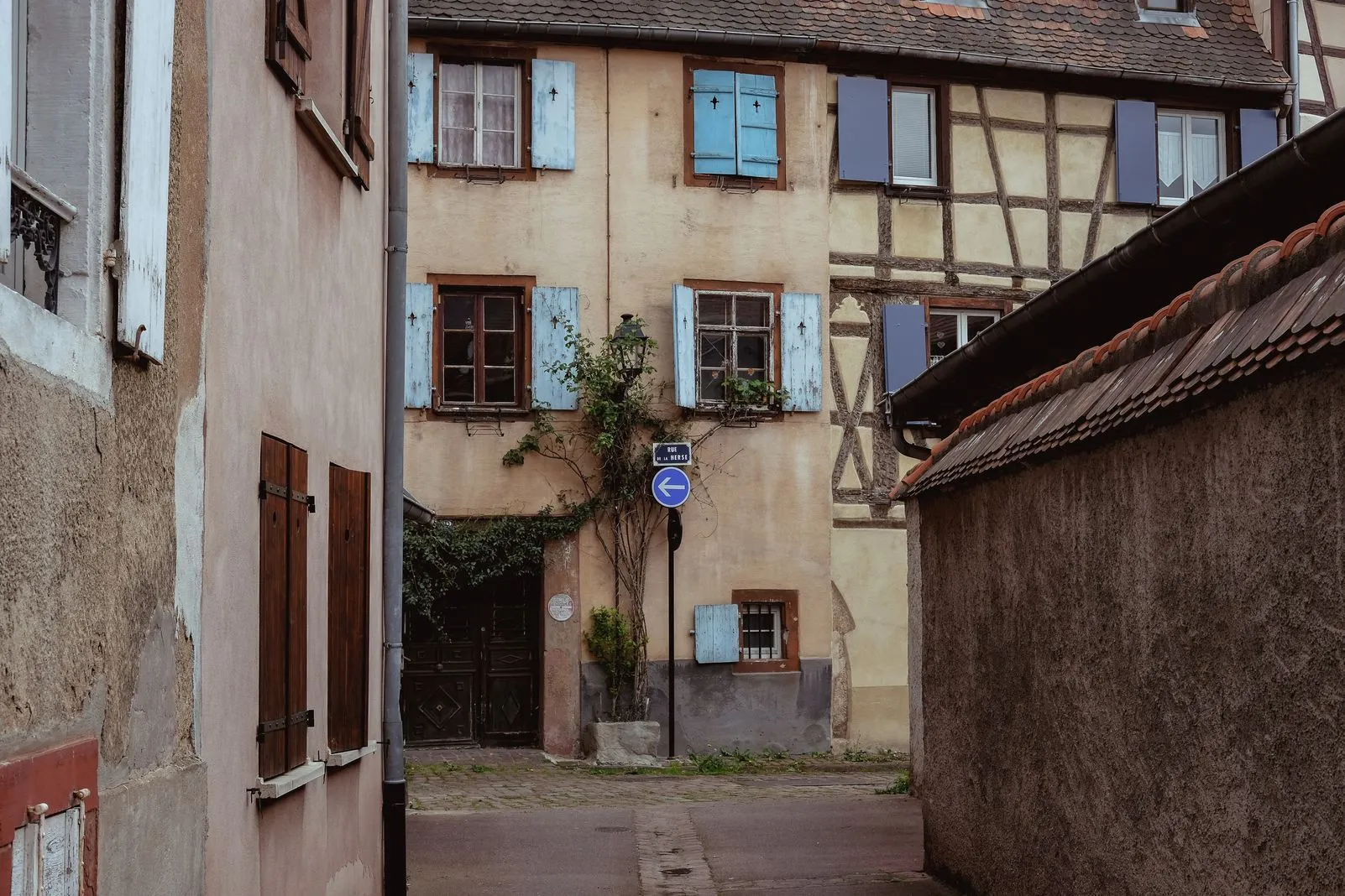 Pastel half-timbered houses with pale blue shutters along a quiet alley