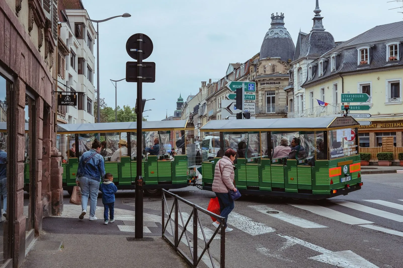 Green tourist trains passing an ornate domed building in a town square