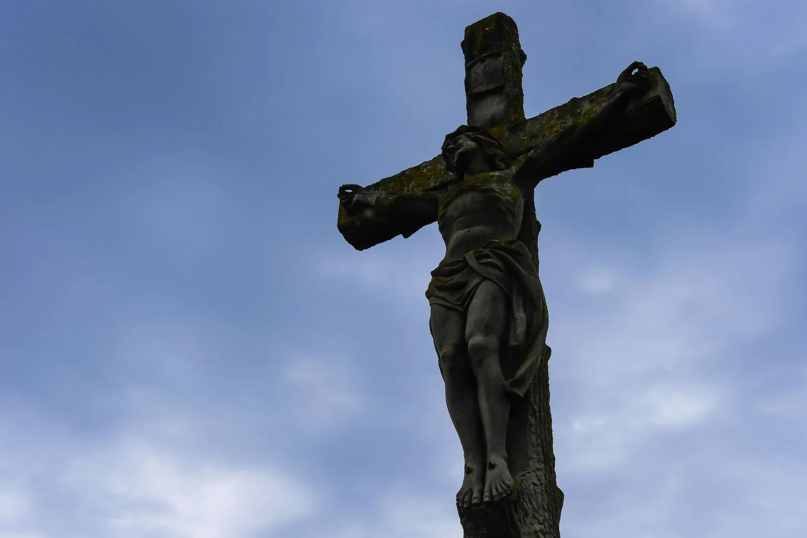A weathered stone crucifix statue set against a clear blue sky