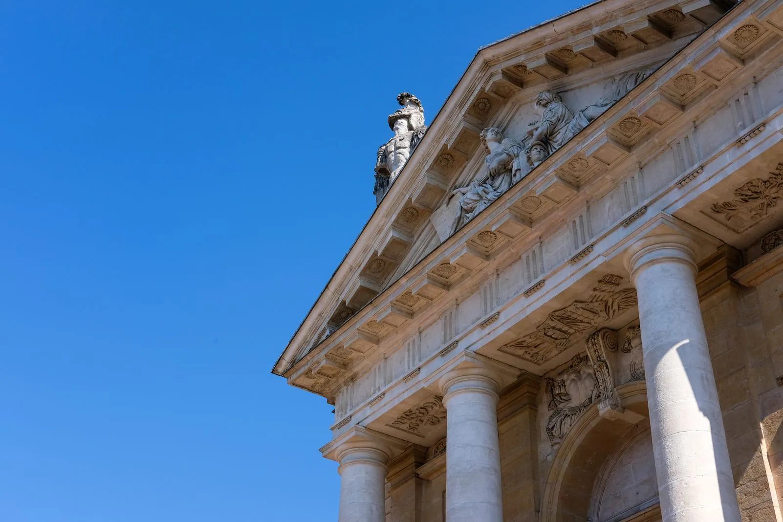 Sculpted figures and columns on a Renaissance palace pediment against a blue sky