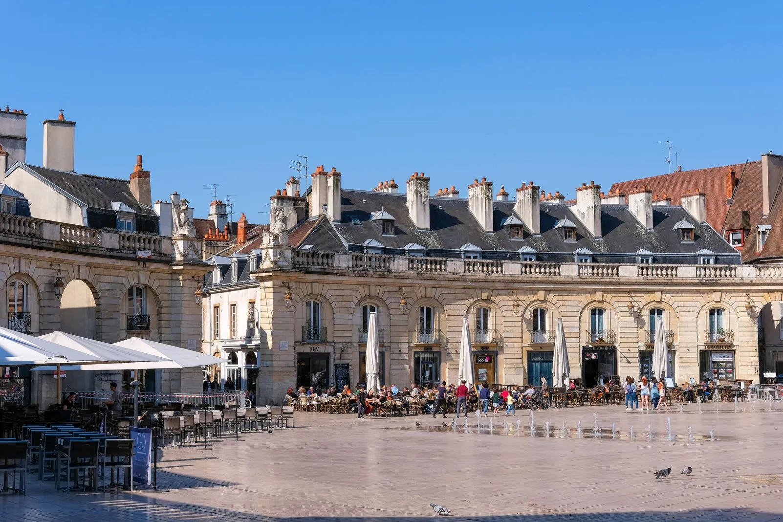 Cafe tables and fountains fill a grand semicircular square lined with historic buildings