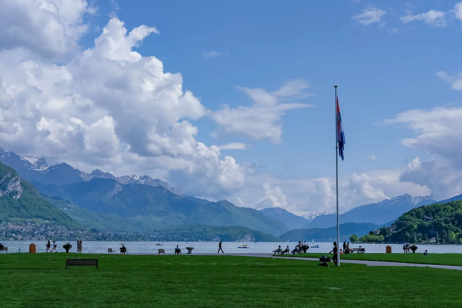 A lakeside lawn with a flagpole overlooking Lake Annecy and the surrounding mountains