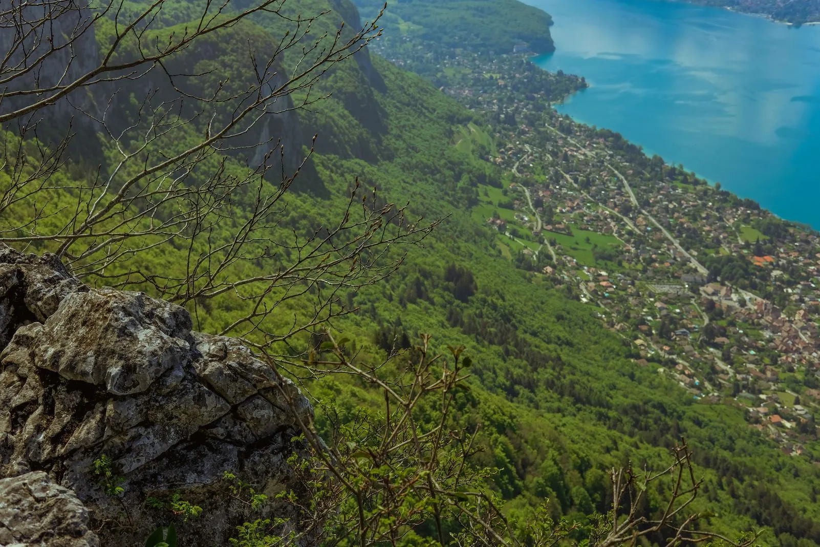 Looking down a forested cliff to a lakeside town along Lake Annecy's turquoise water