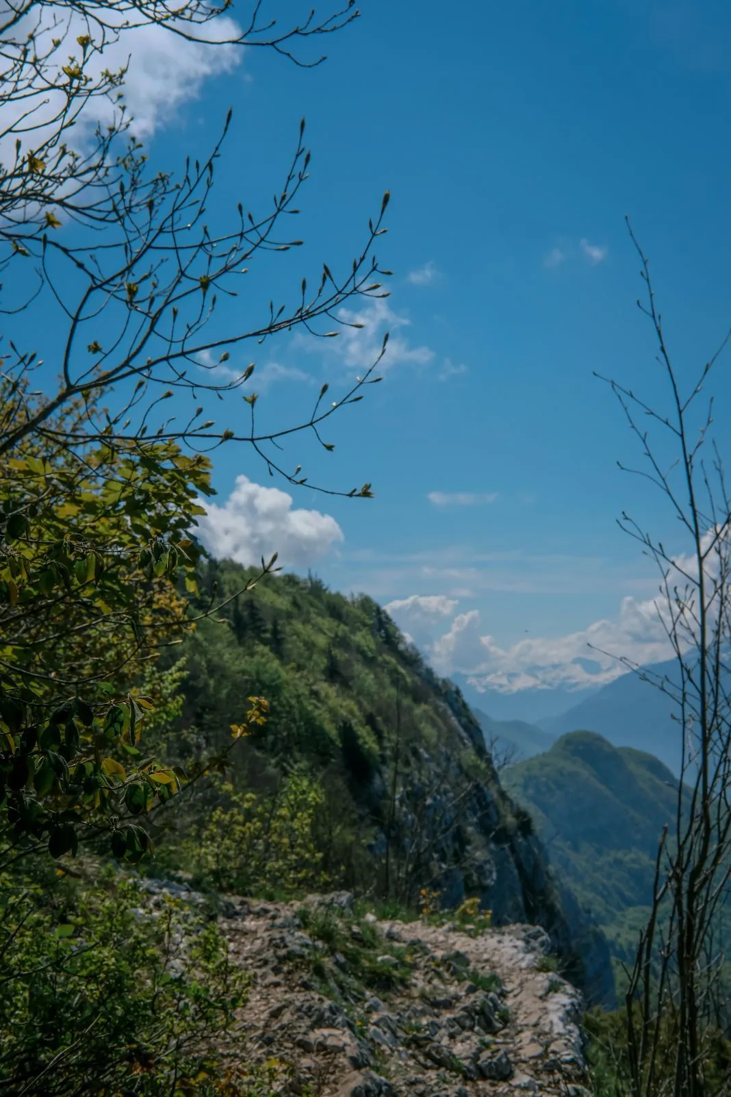 A rocky mountain trail winds along a sheer cliff edge under a bright sky
