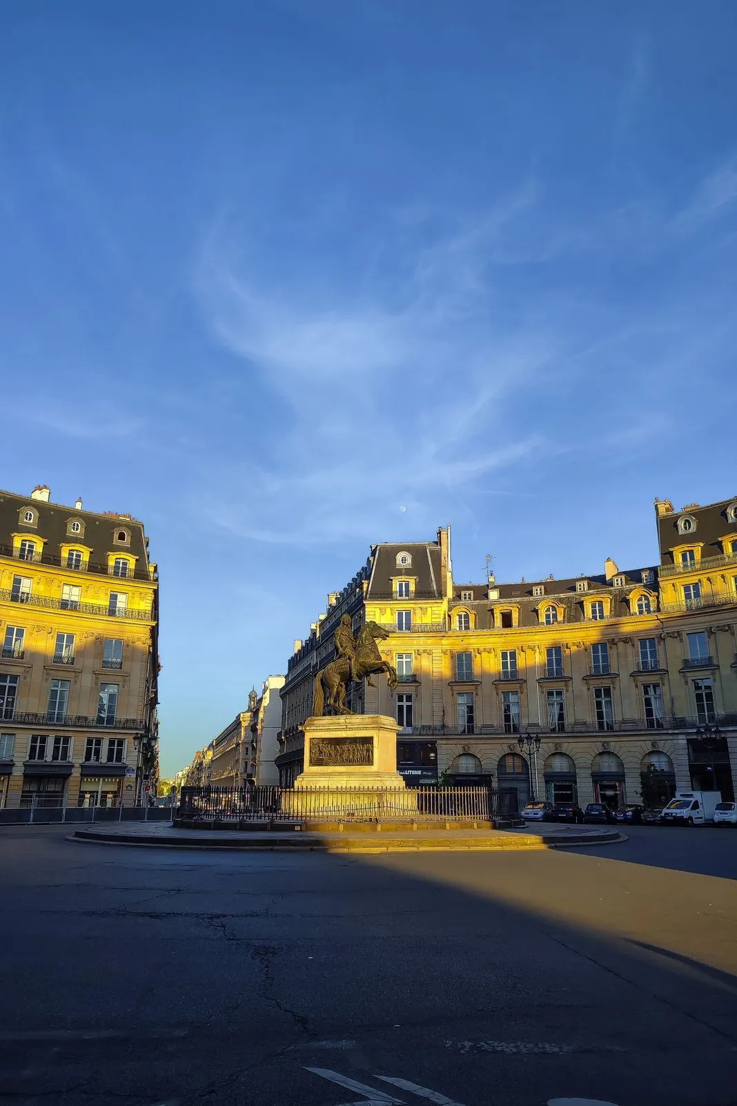 A bronze equestrian statue glows gold at sunrise in a grand Parisian square