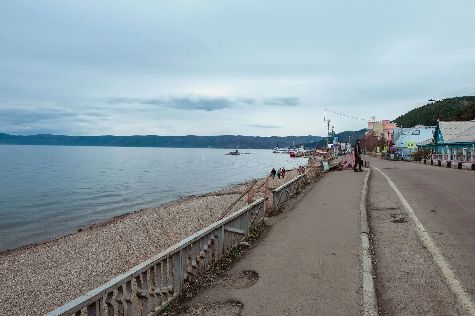 Pebble beach promenade along Lake Baikal with a hillside village and moored boats