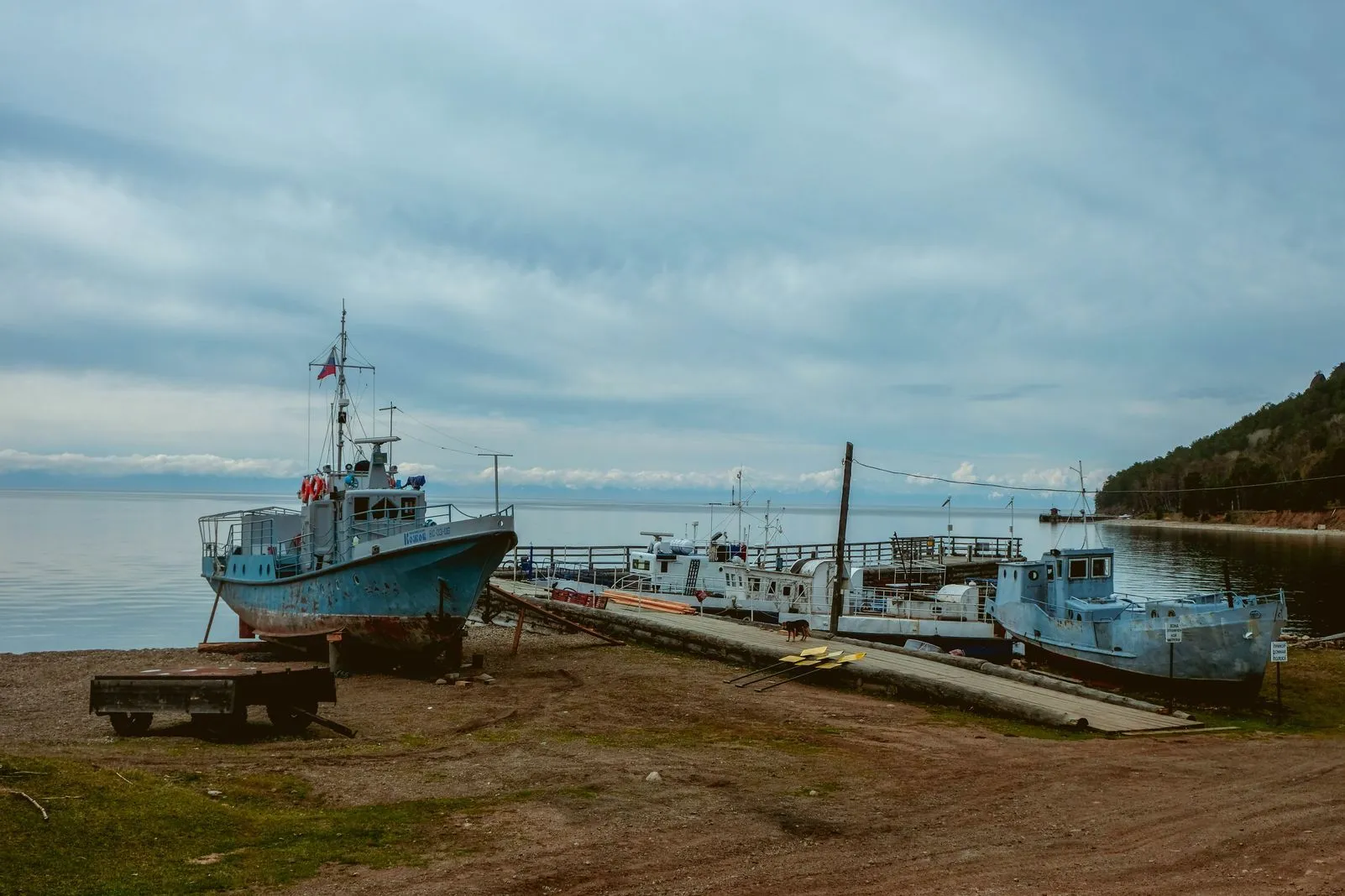 Old fishing boats pulled up on shore beside a wooden dock
