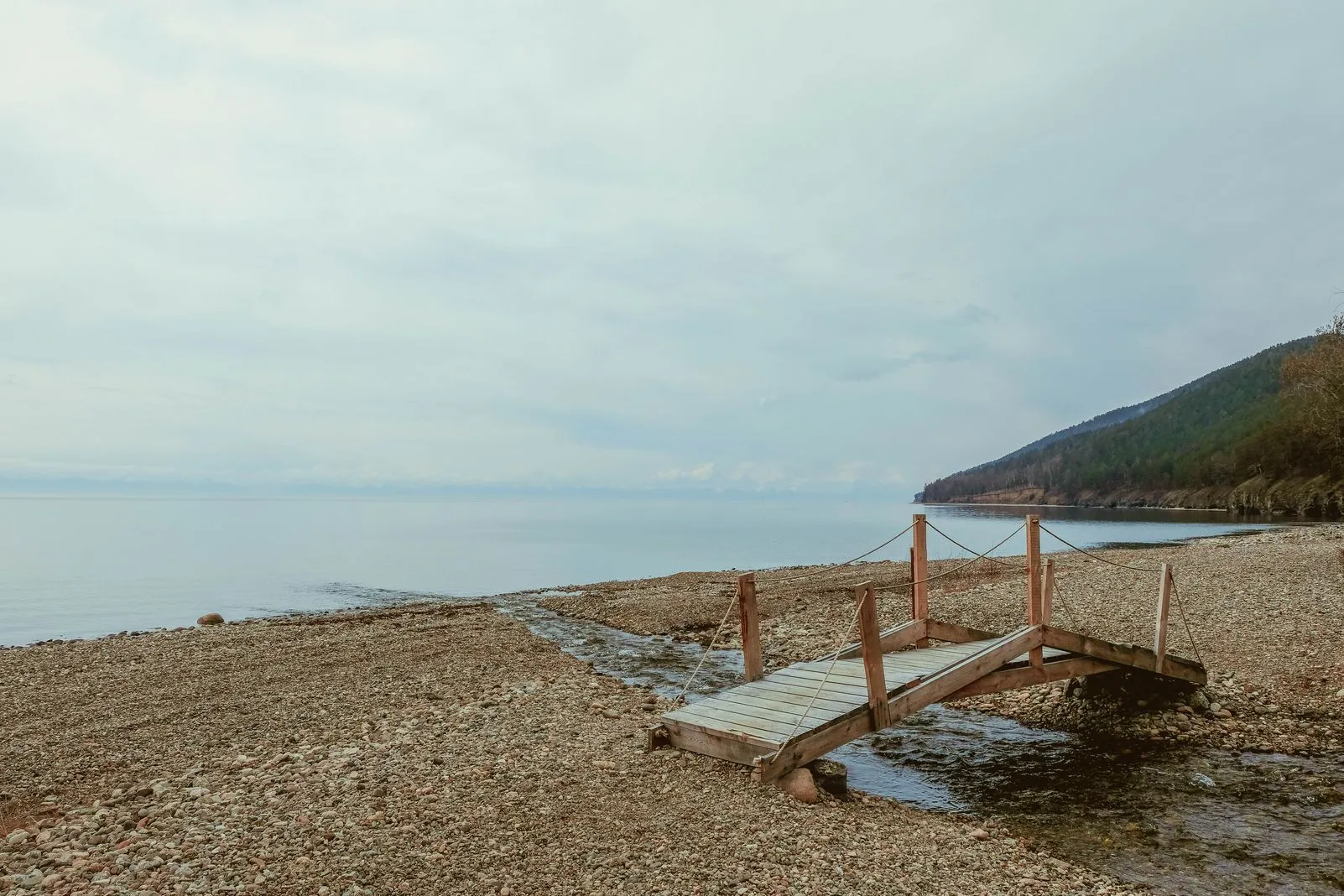 Wooden footbridge crossing a stream on a pebble beach