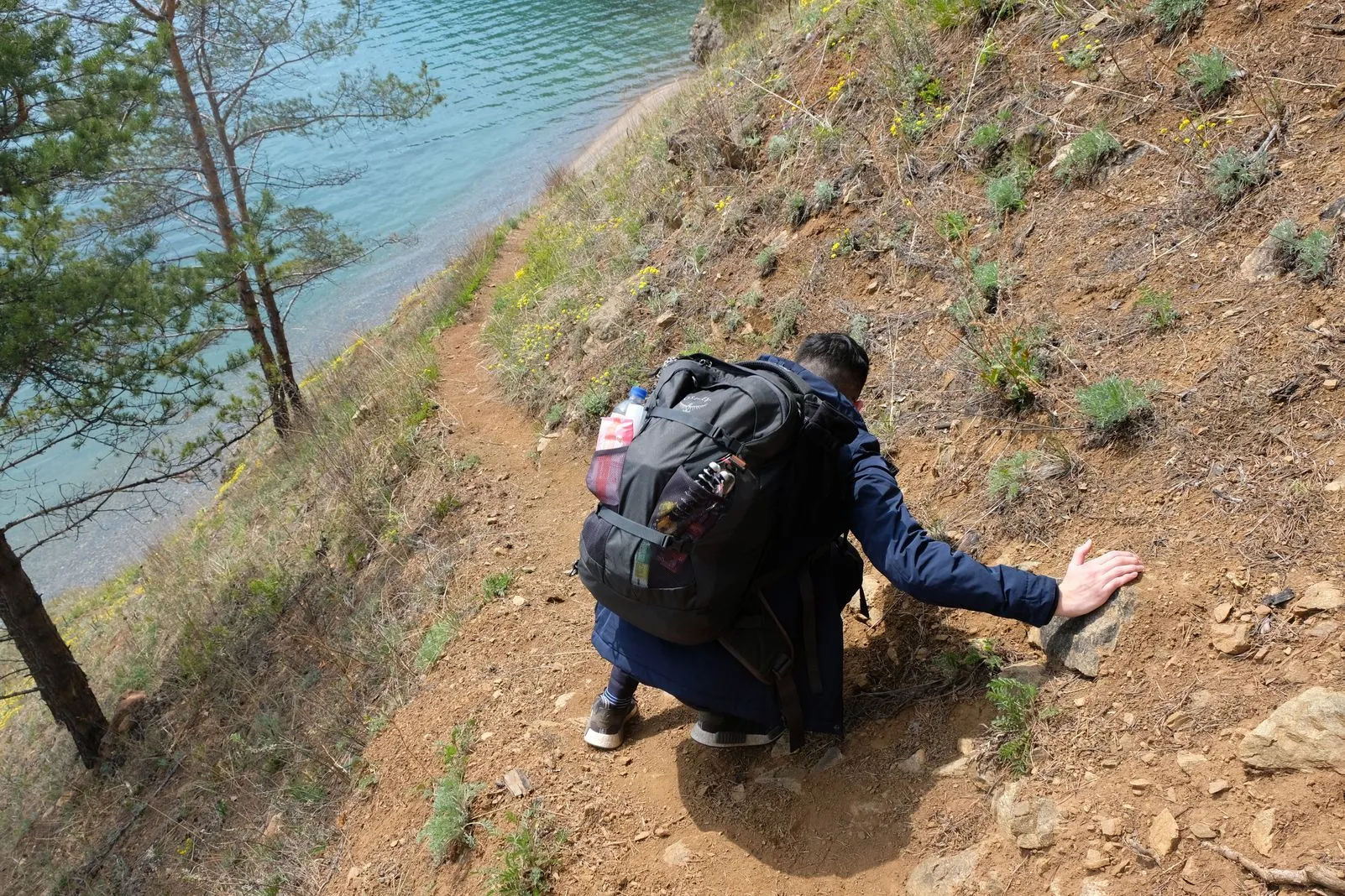Hiker with a large backpack scrambling down a steep dirt trail