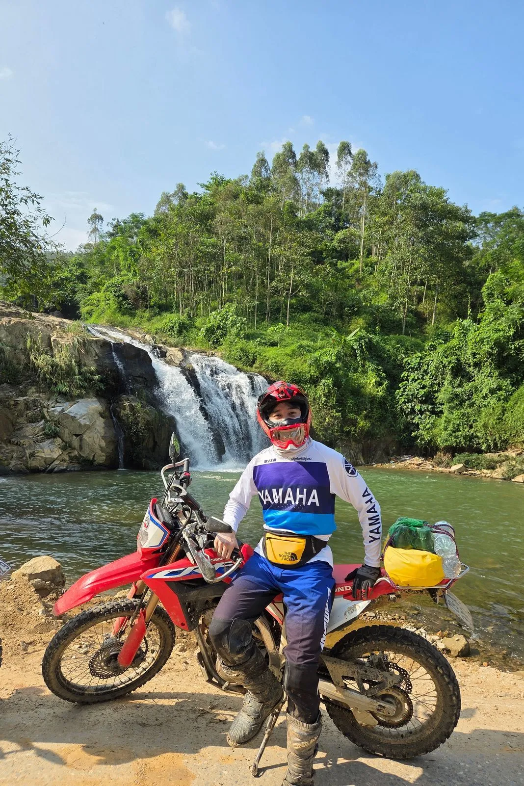 Rider in a Yamaha jersey sitting on a dirt bike in front of a jungle waterfall