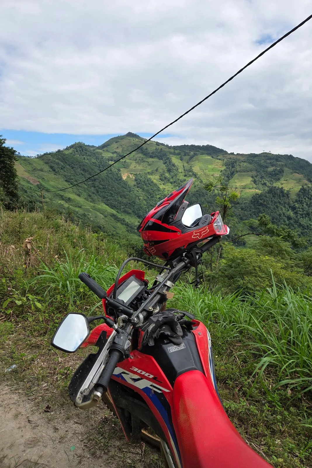 Red Fox helmet perched on the handlebars of a dirt bike above misty green mountains