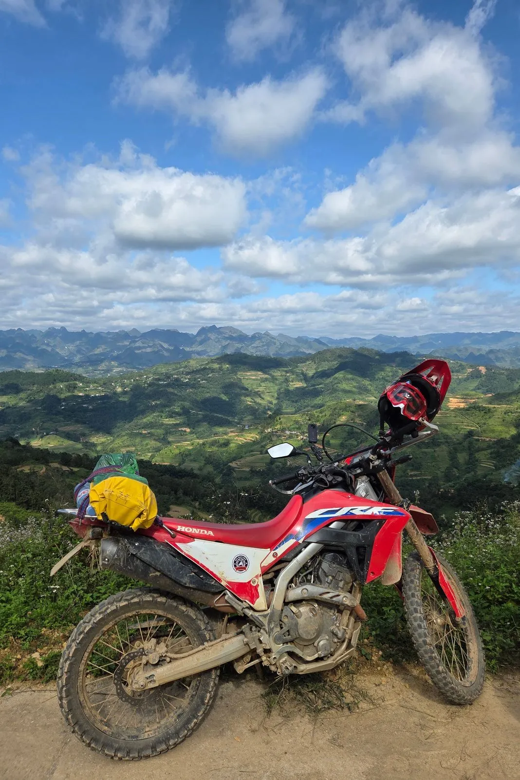 Loaded Honda CRF dirt bike parked on a ridge overlooking terraced green valleys