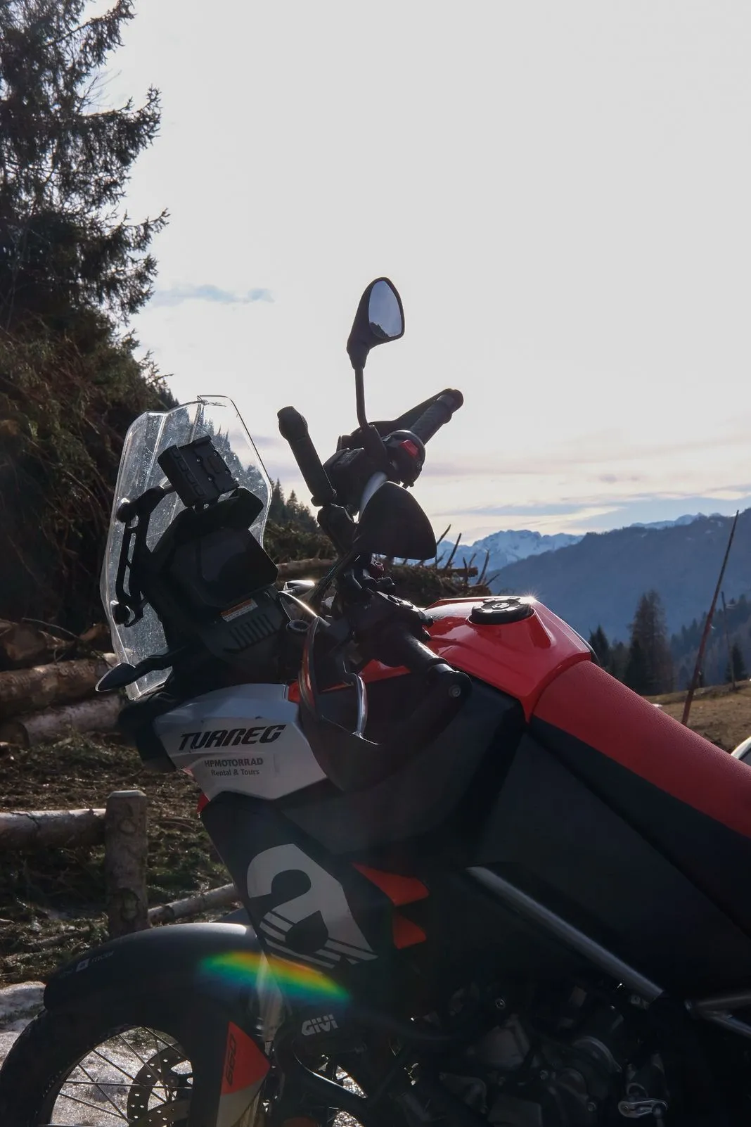 Close-up of an Aprilia Tuareg's tank and cockpit backlit by the sun over snowy peaks